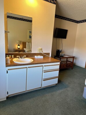 A hotel bathroom with a sink, mirror, and a television mounted on the wall.