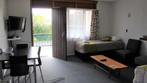 A compact room with a bed, a sofa, a small table, a TV, and a balcony with a view. - Elmore Lodge Motel (Hastings)