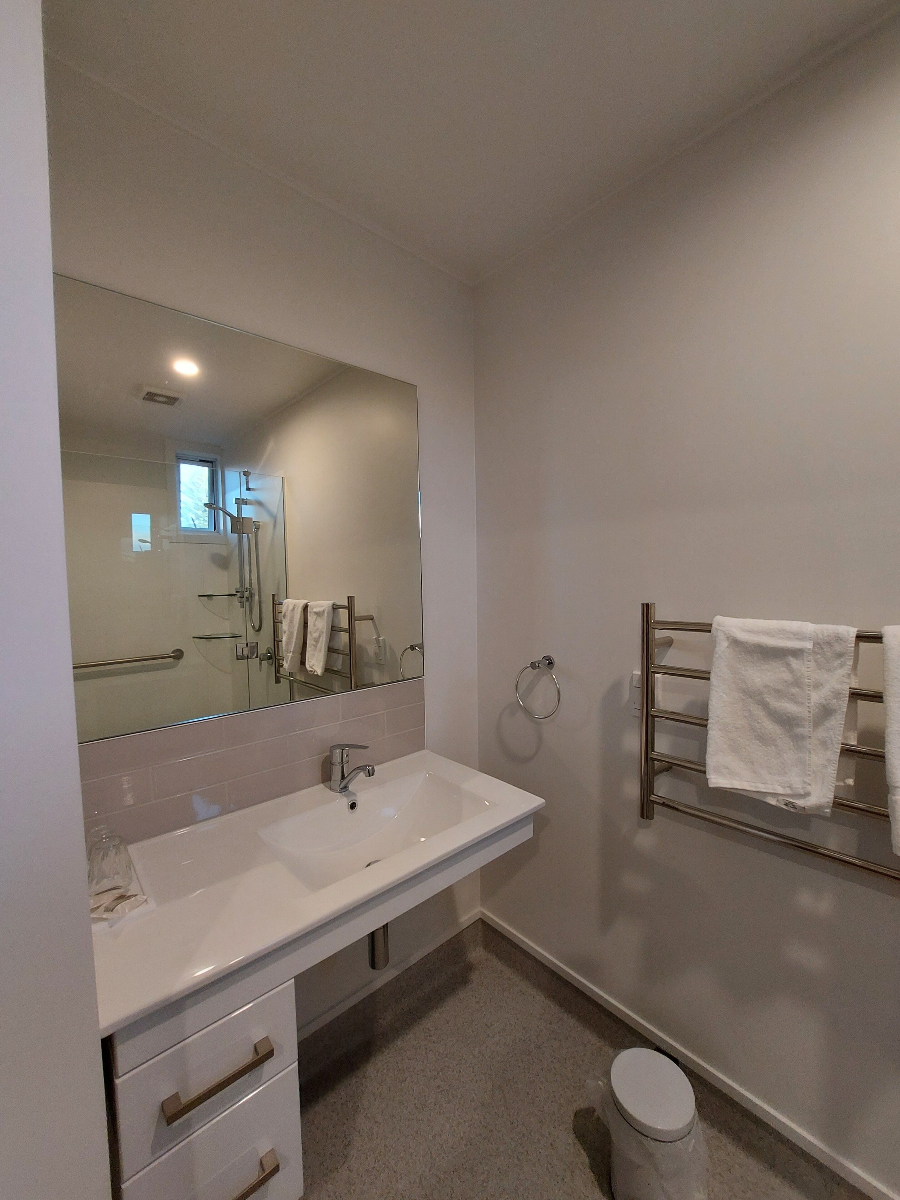 Een moderne badkamer met een grote spiegel, een wit wastafelmeubel, een handdoekrek en een toilet.