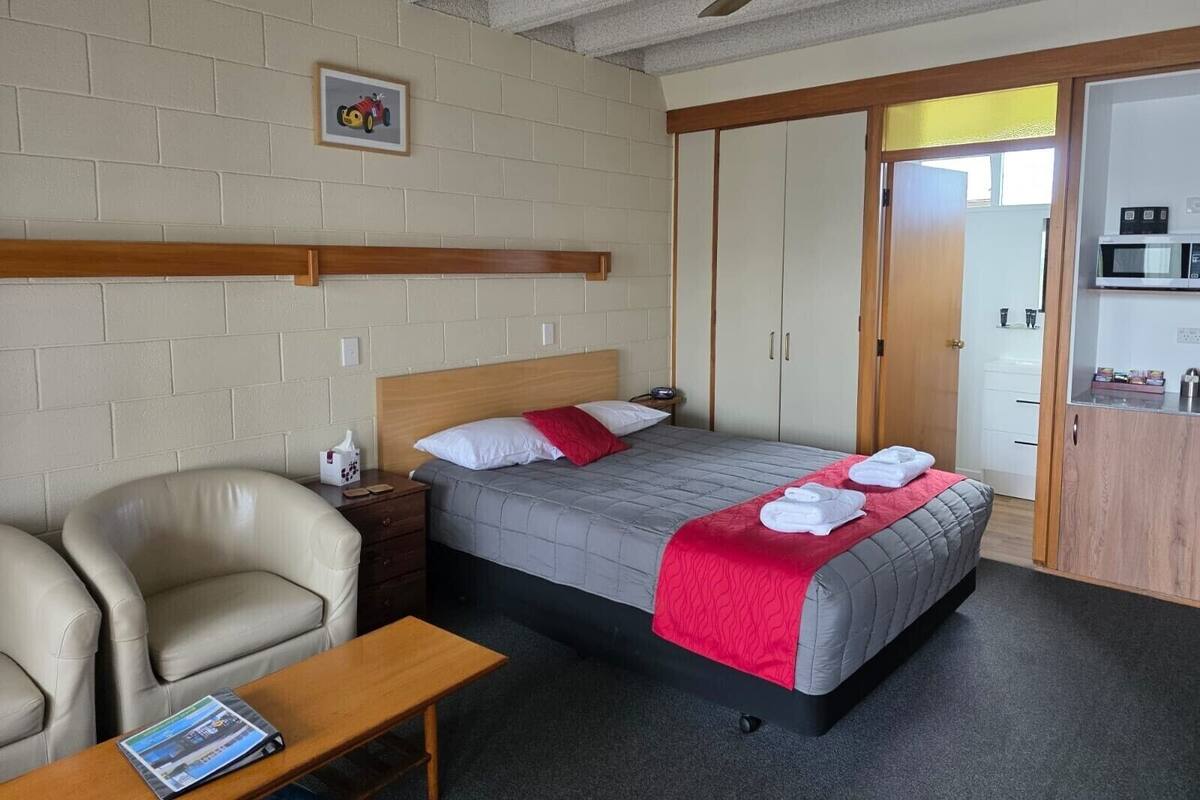 A hotel room with a bed, a chair, a table, a wardrobe, and a ceiling fan.