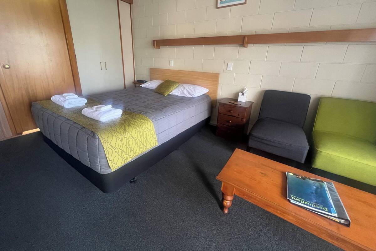 A hotel room with a bed, a nightstand, a green armchair, and a wooden coffee table.