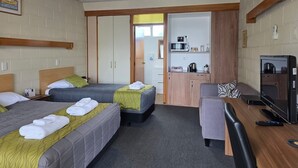 A hotel room with two beds, a desk, a television, and a kitchenette. - Elmore Lodge Motel (Hastings)