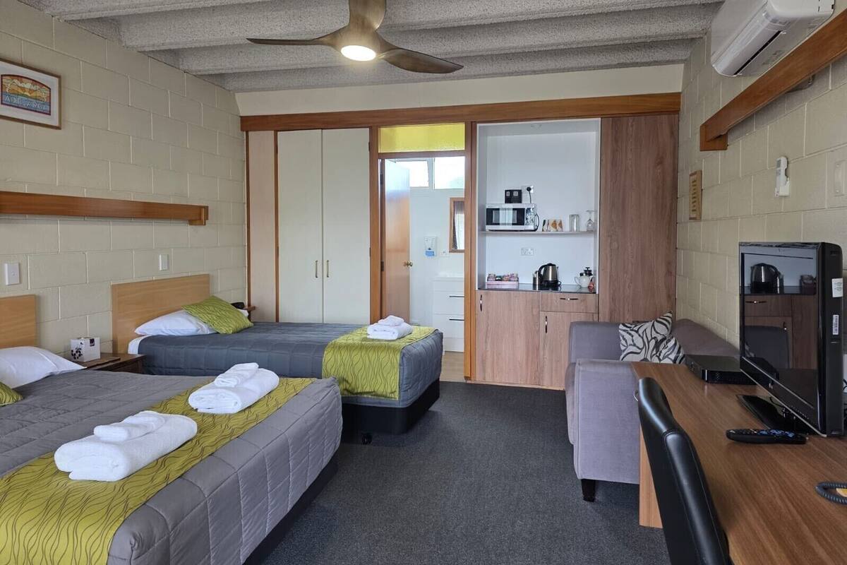 A hotel room with two beds, a desk, a television, and a kitchenette.