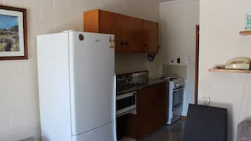 Eine kleine Küche mit Holzausstattung, einem weißen Kühlschrank, einem Herd und einer Mikrowelle.