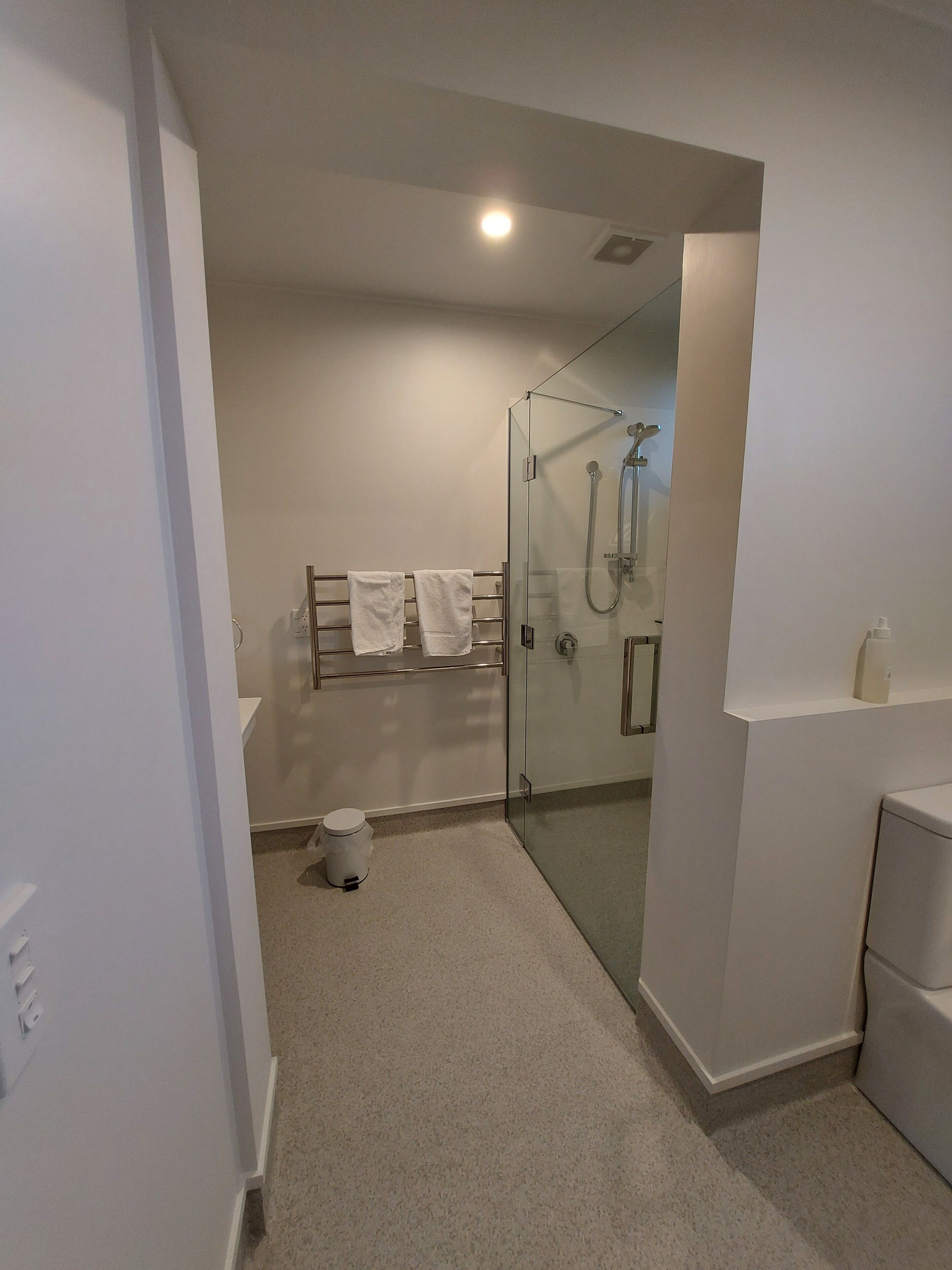 Un bany modern amb un espai de banyera de vidre, un lavabo blanc i un suport per a tovalloles.