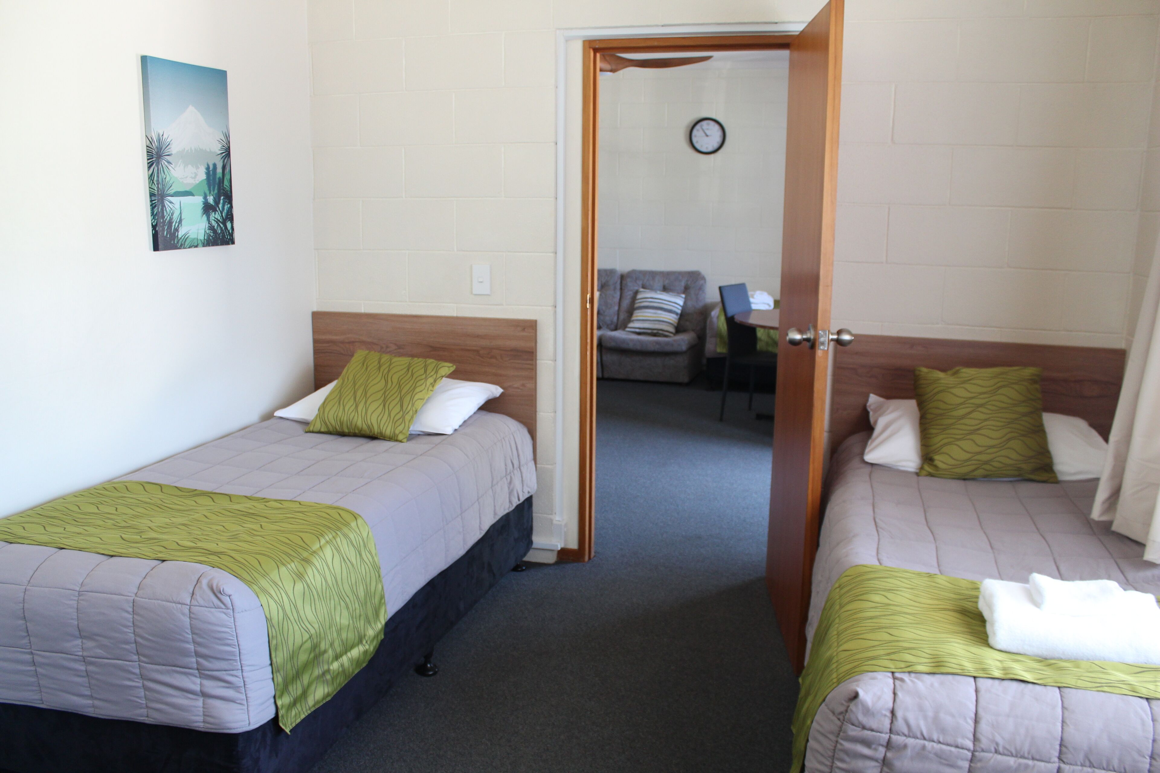 Two single beds with green and white bedding, a wooden headboard, and a painting on the wall.