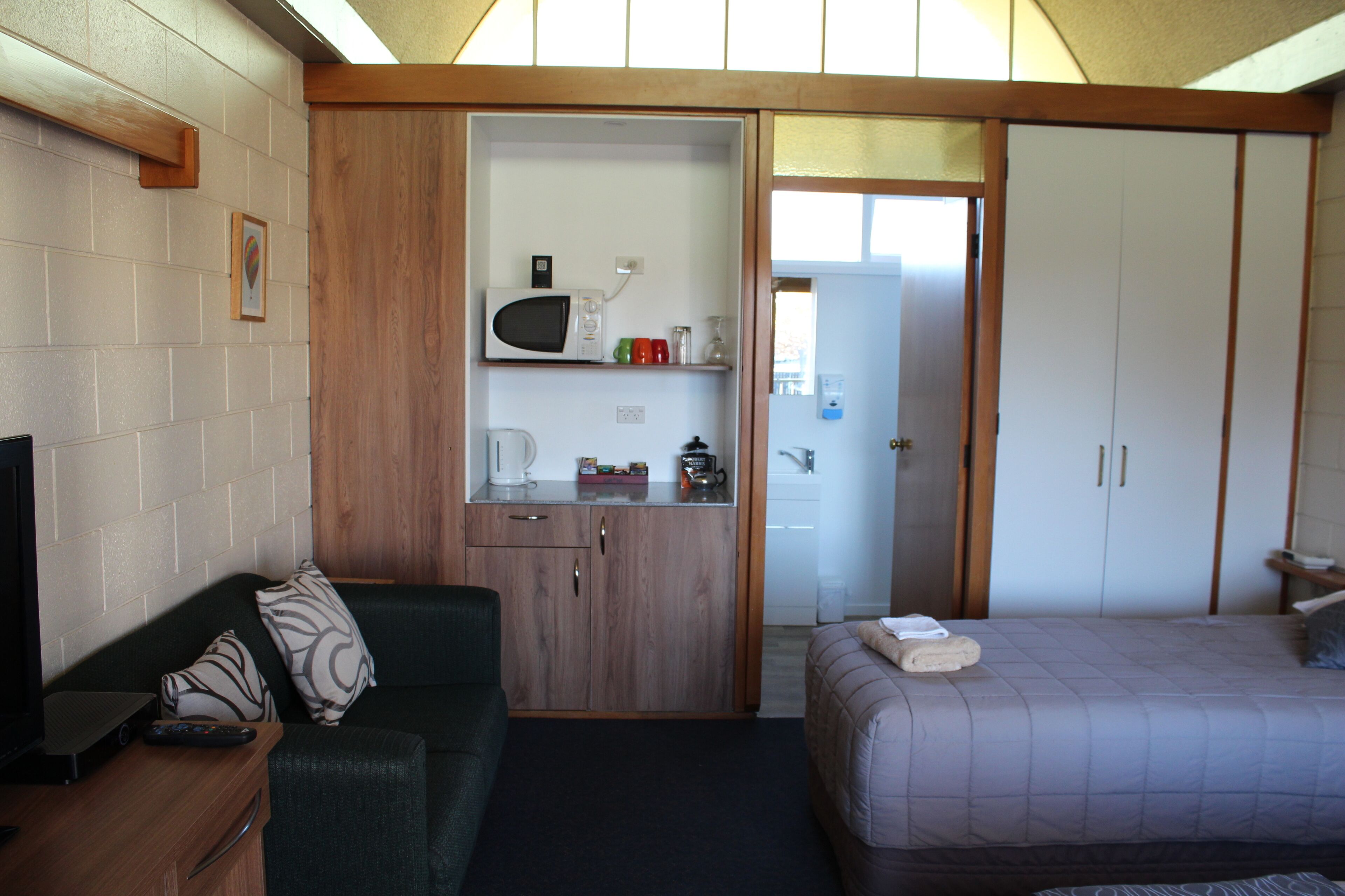 A compact room with a bed, a sofa, a kitchenette, and a television.