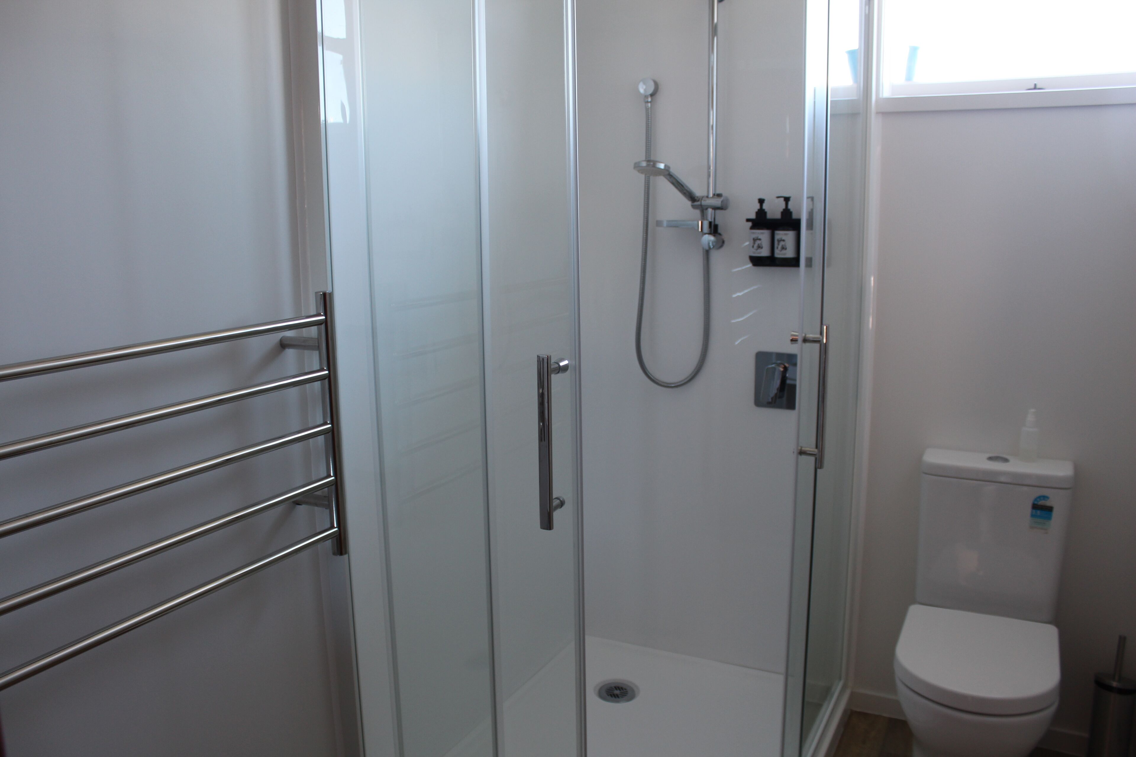 A modern bathroom with a glass-enclosed shower, a toilet, and a metal towel rack.