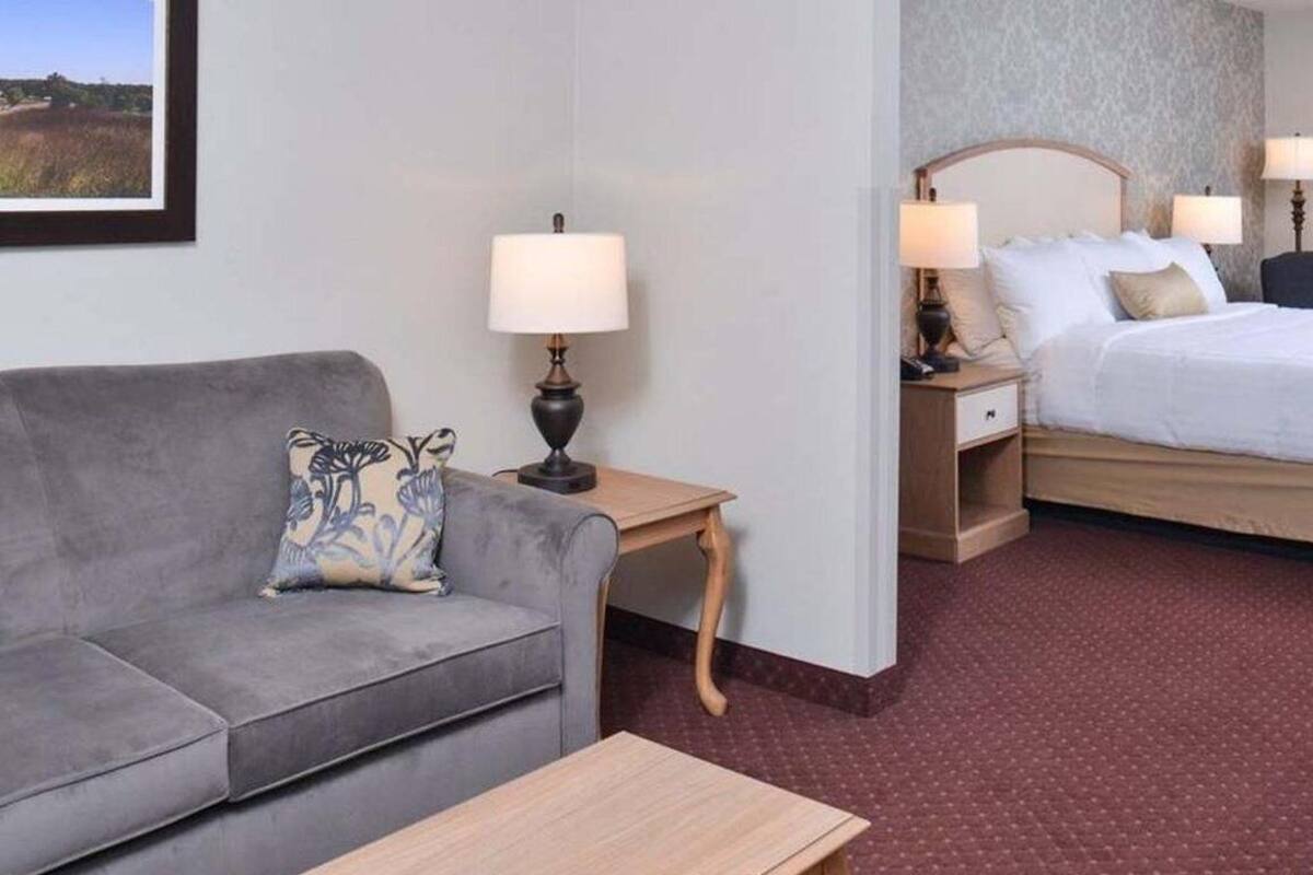 Ein Hotelzimmer mit grauem Sofa, einem Holztisch, einem Bett mit weißer Bettwäsche und zwei Nachttischlampen.