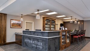 A reception area with a marble counter labeled "Appomattox Inn & Suites," a wooden cabinet with glass doors, and a dining area with red chairs. - Appomattox Inn and Suites (Appomattox)