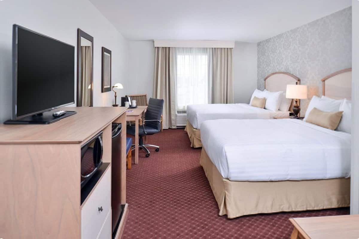 Una habitación de hotel con dos camas, un escritorio con computadora, un televisor y una silla.