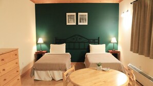 Una habitación con dos camas, un aparador de madera, una mesa redonda y una planta pequeña.