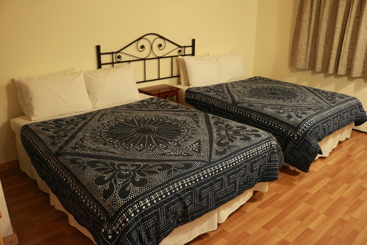 Une chambre double avec deux lits, chacun agrémenté de draps à motifs, dotée d’un plancher en bois et d’une tête de lit ornée d’un motif décoratif.