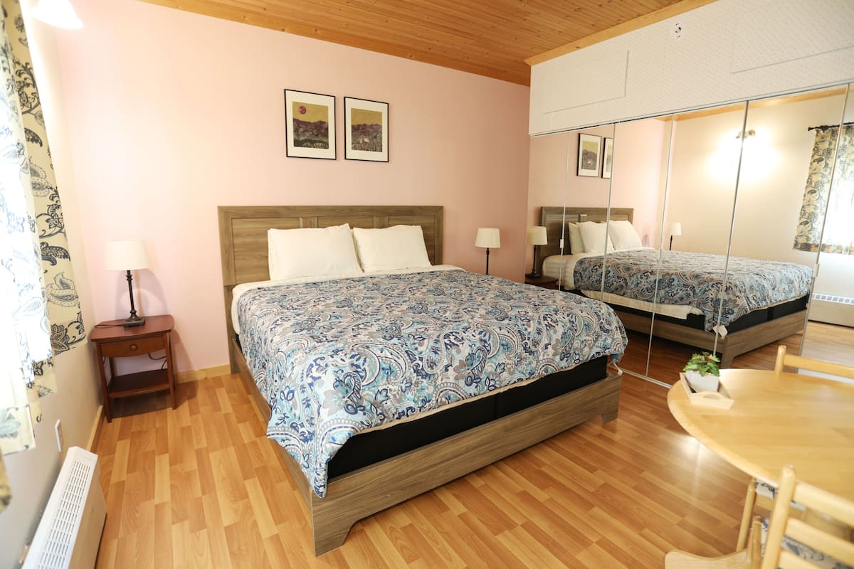 Une chambre avec deux lits, un plancher en bois, une petite table et un miroir.