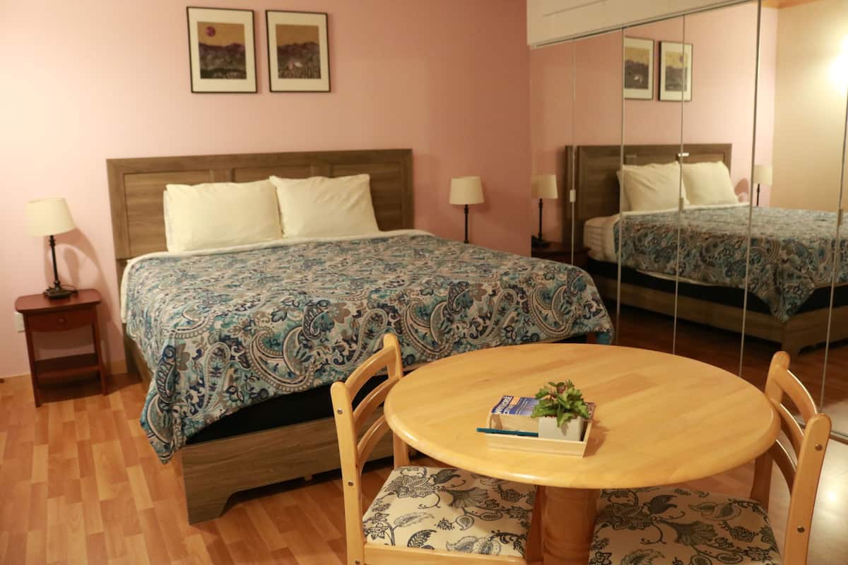 Une chambre avec un lit double, une table de chevet avec une lampe, une table ronde en bois avec des chaises et un miroir au mur.