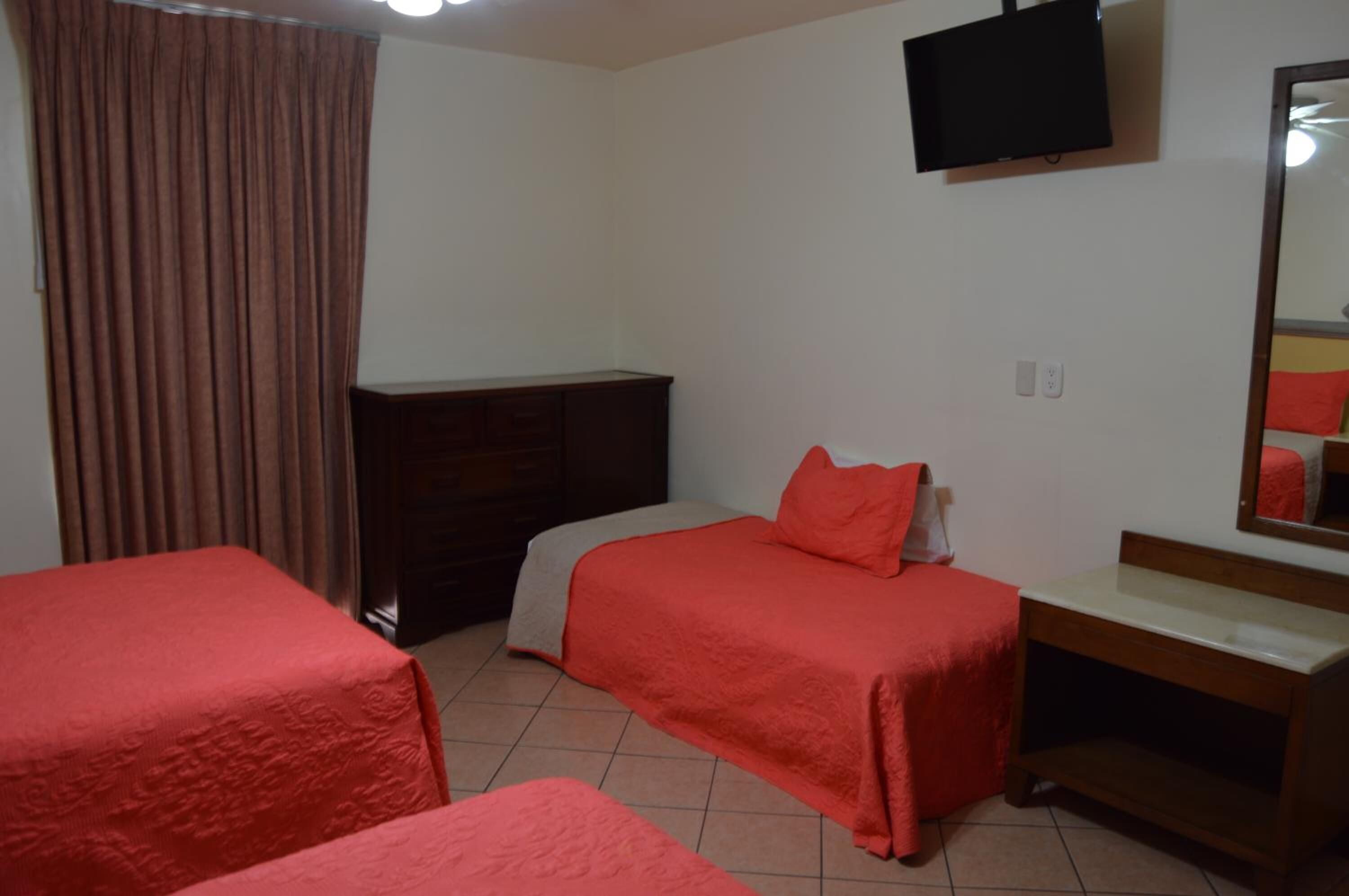 A hotel room with two beds, a TV mounted on the wall, a wooden dresser, and a mirror.
