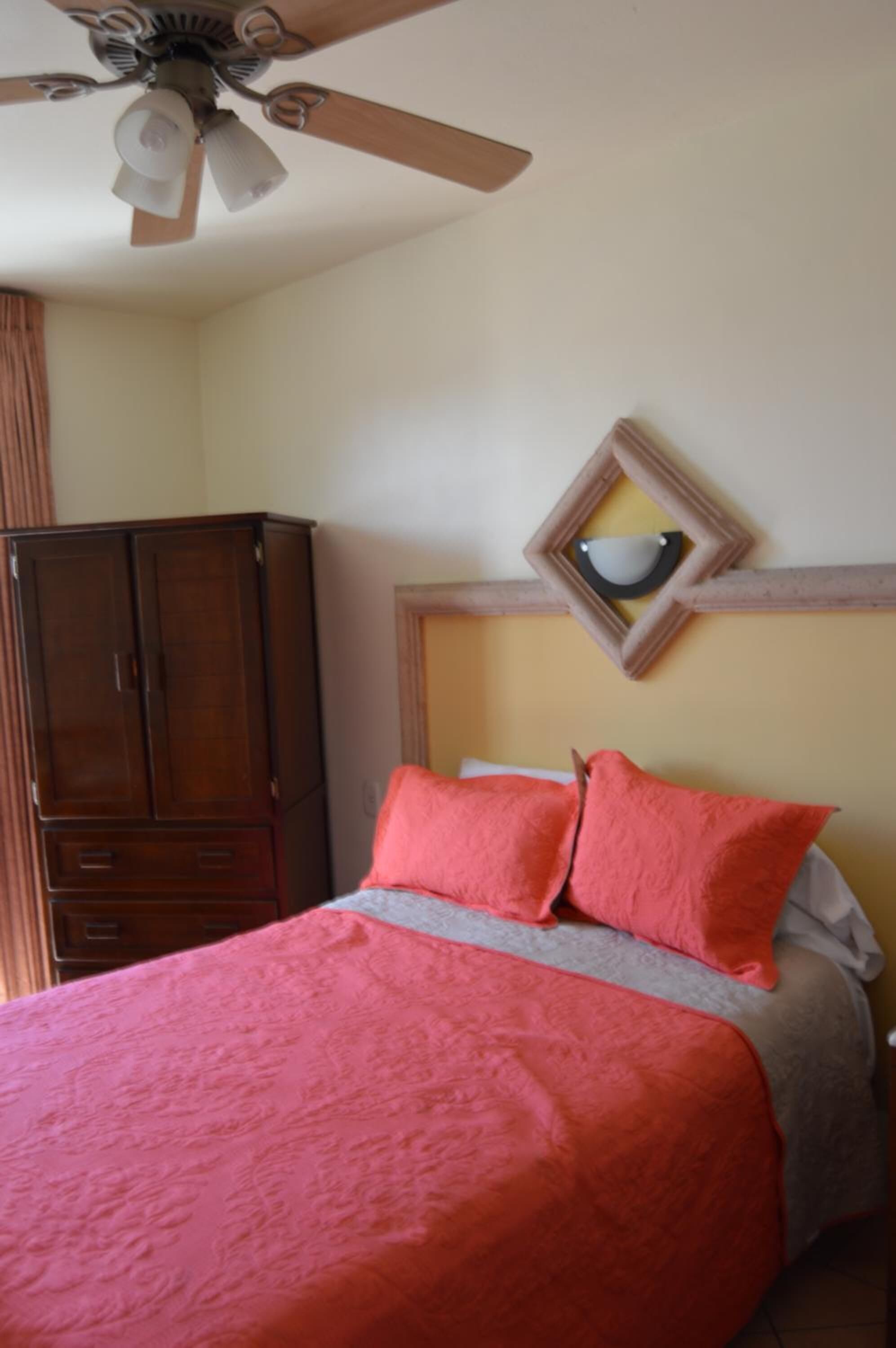A bedroom with a bed, a ceiling fan, a wardrobe, and a wall-mounted mirror.