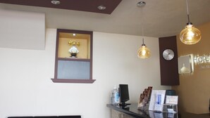 Zona de recepción de hotel con mostrador, reloj, ventana con adorno y lámparas colgantes.
