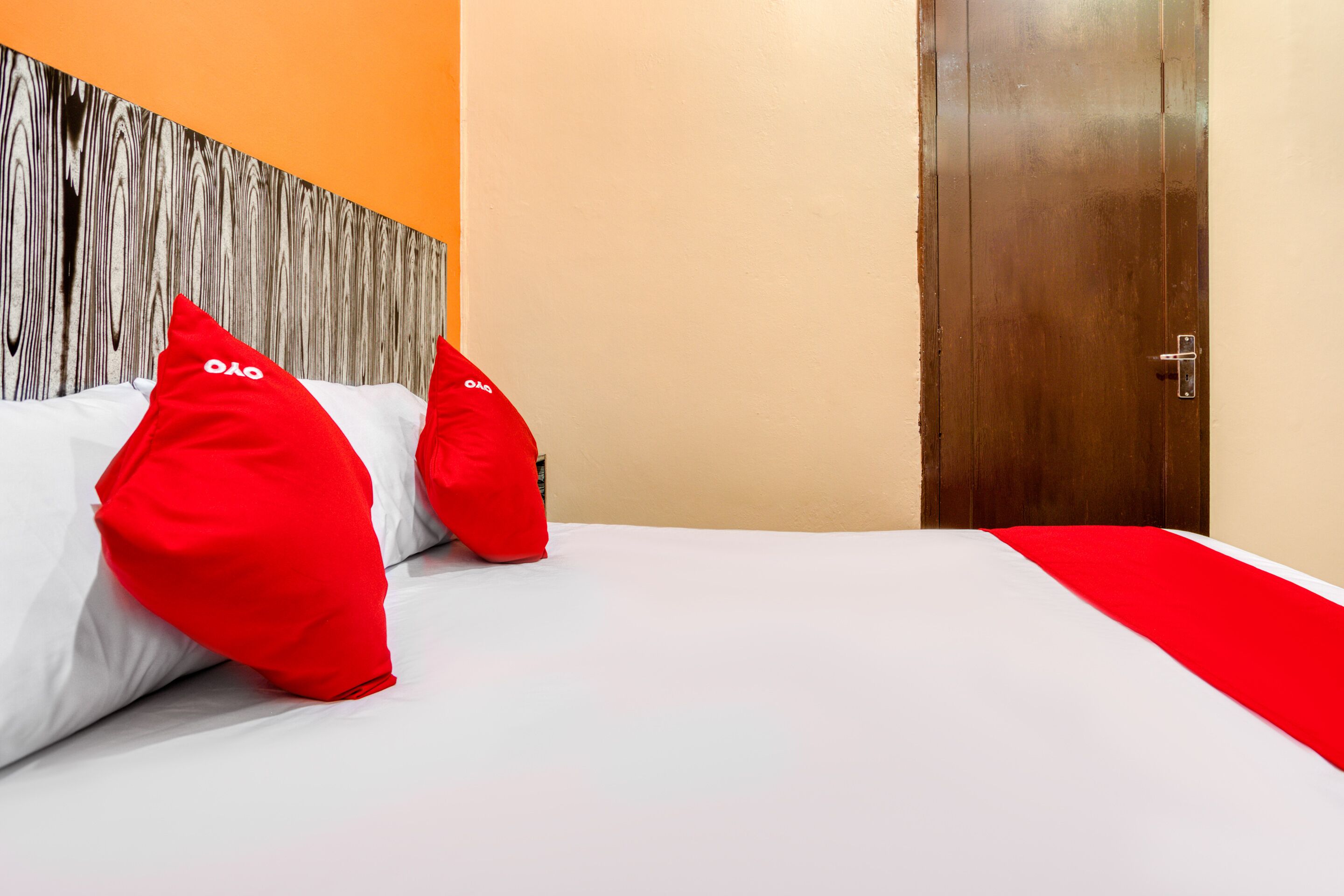 A hotel room with a wooden headboard, a white bedspread, and red pillows.