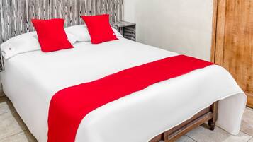 Una cama bien hecha con ropa de cama blanca y roja, cabecera de madera y suelo de baldosas.