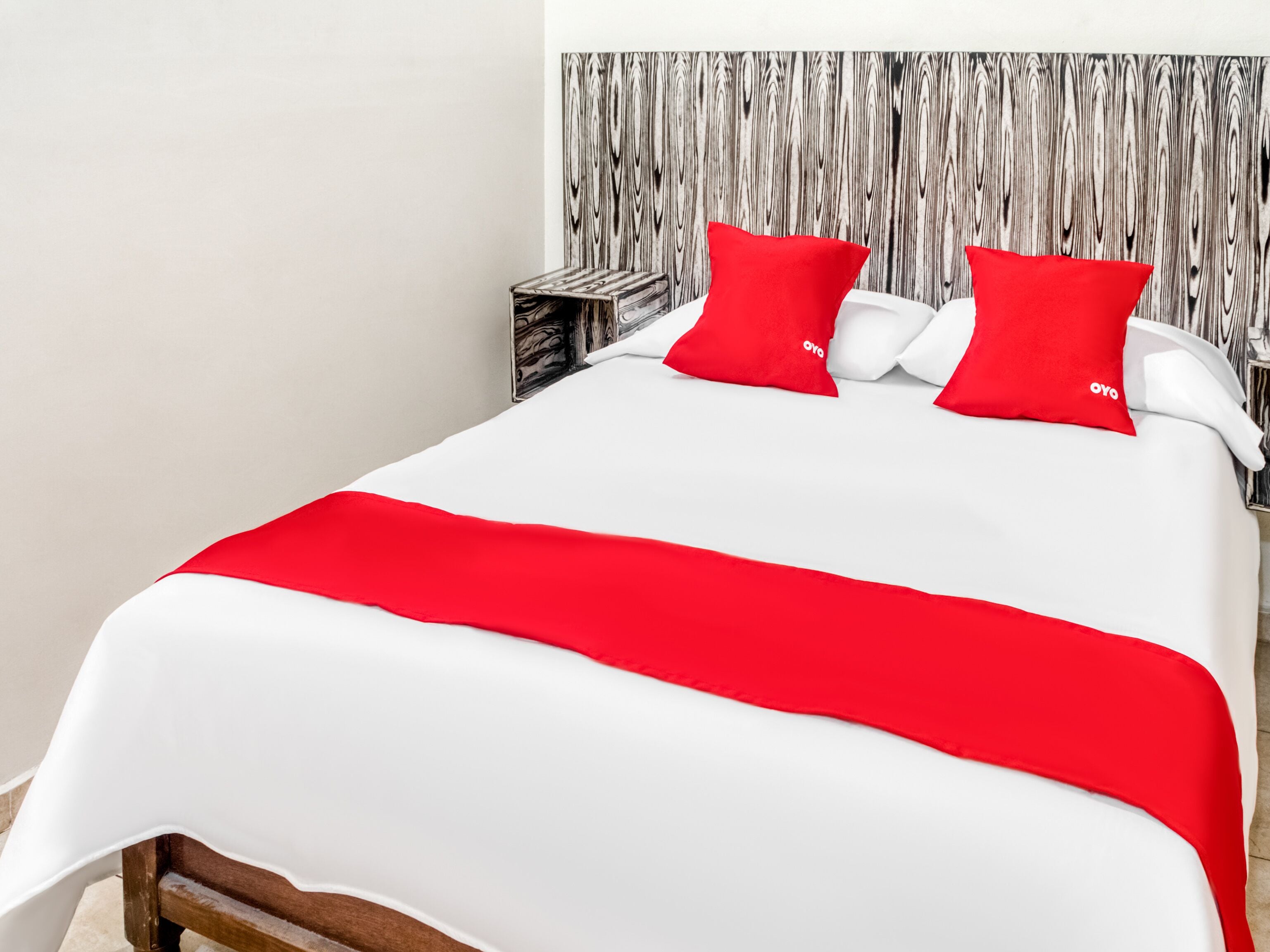 A bed with a white and red bedspread, two red pillows, and a wooden headboard.