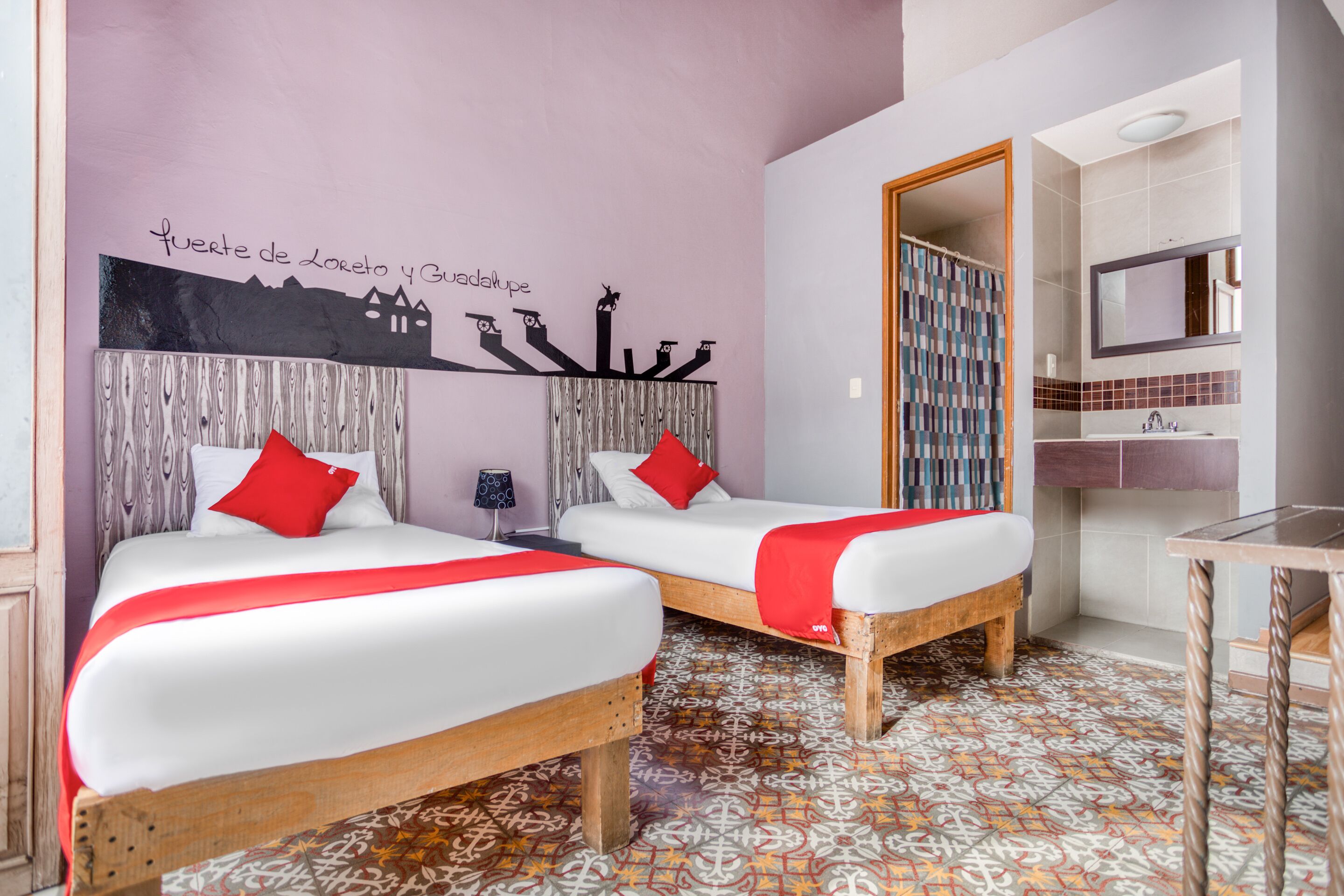 A hotel room with two beds, a bathroom, and a wall mural.