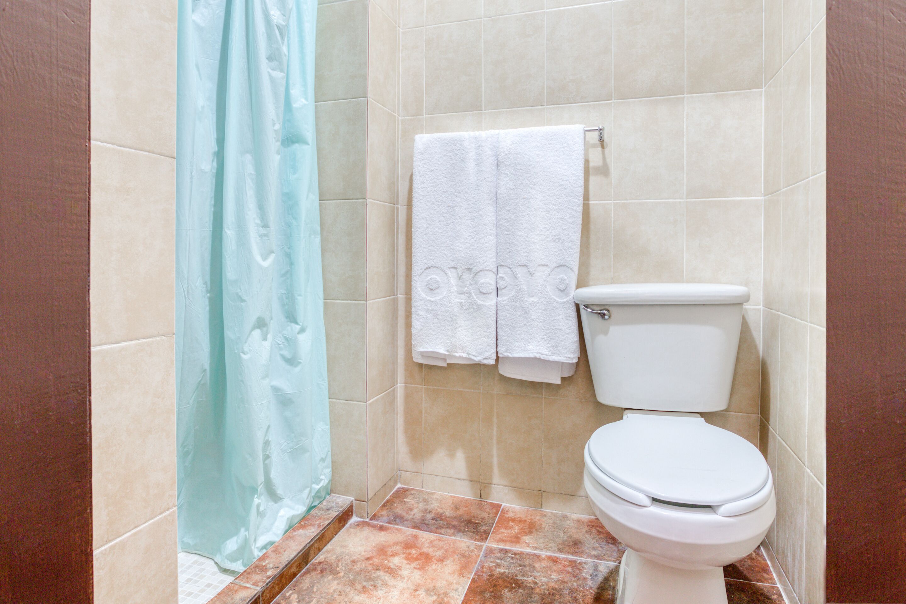 A bathroom with a toilet, two white towels hanging on the wall, and a blue shower curtain.