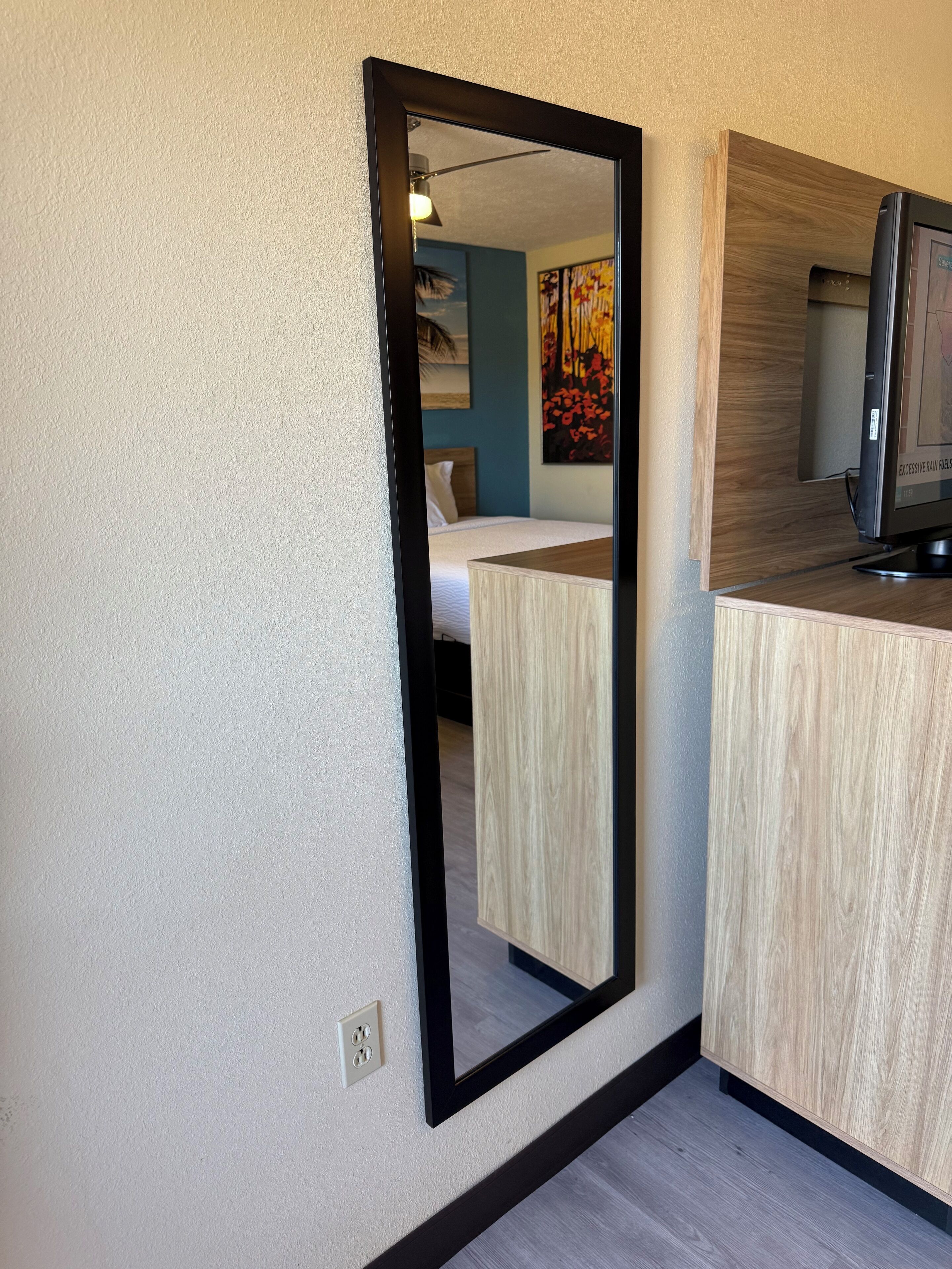 A room with a bed, a wooden desk, and a mirror on the wall.