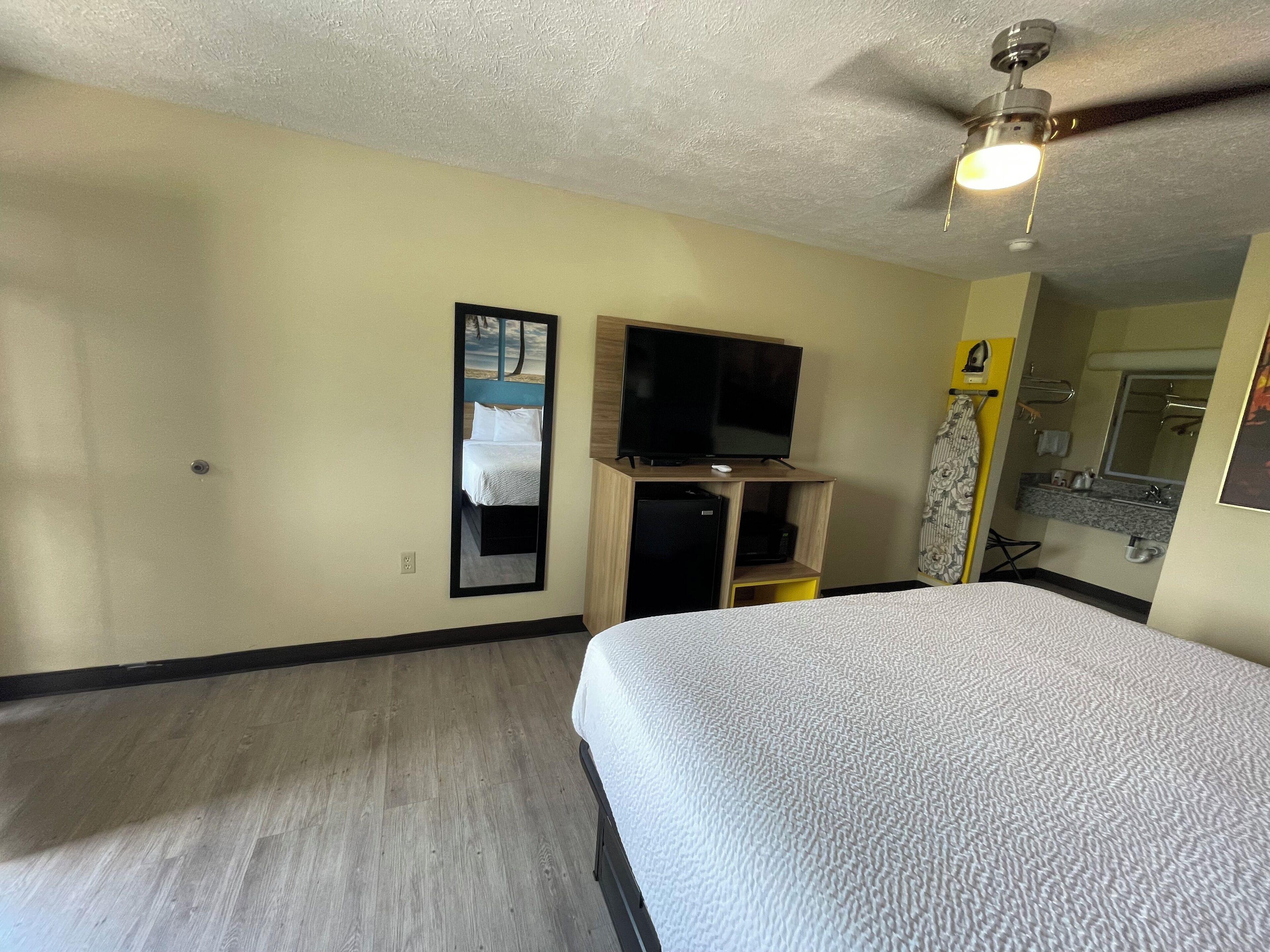 A hotel room with a bed, a television, a ceiling fan, and a bathroom with a mirror and sink.