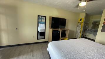 A hotel room with a bed, a television, a ceiling fan, and a bathroom with a mirror and sink.