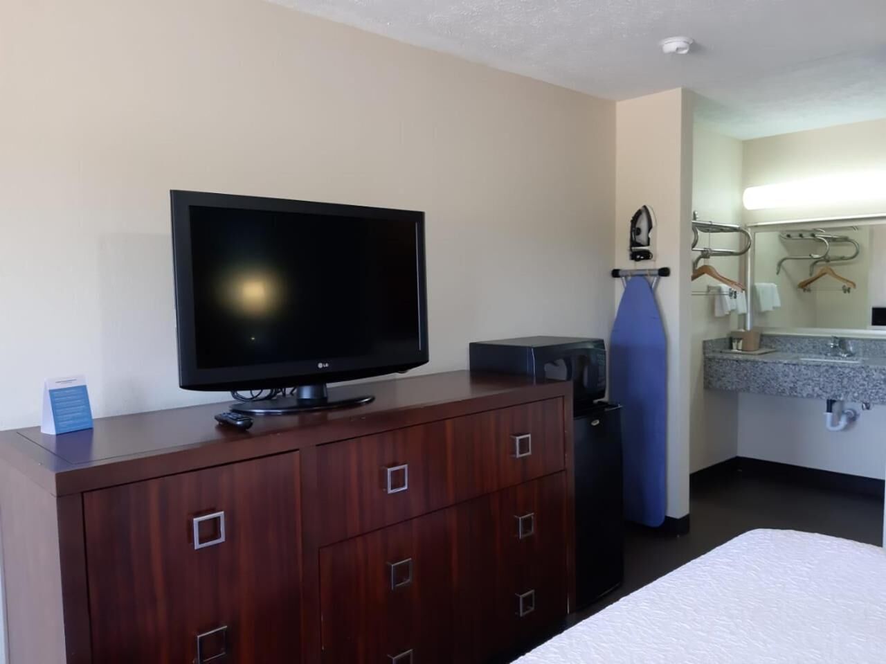 A hotel room with a TV on a wooden dresser, a bed, a bathroom with a mirror, and a blue ironing board.