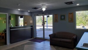 A reception area with a desk, a couch, and a door leading outside. - Deerfield Inn (Parsons)
