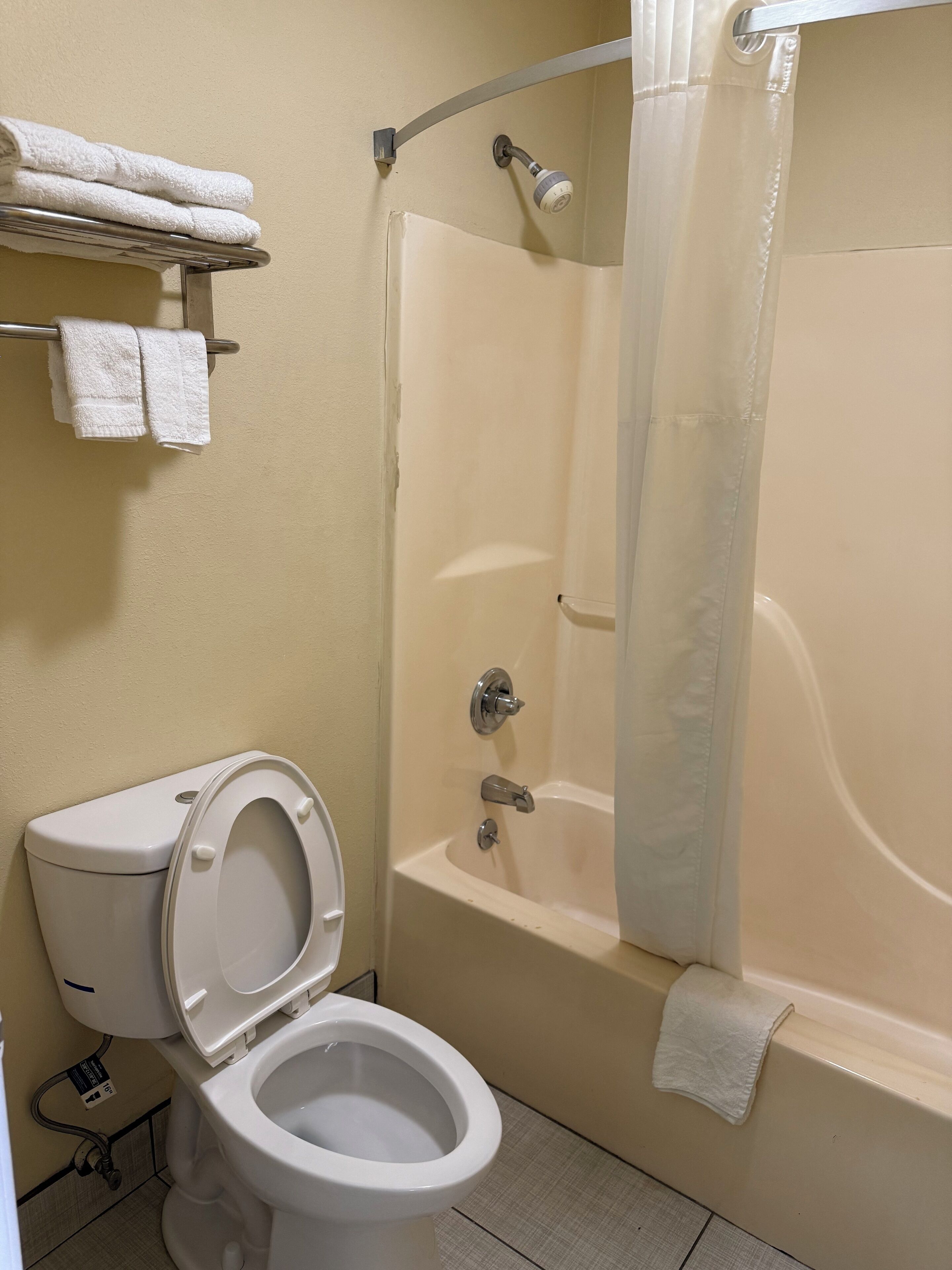 A bathroom with a toilet, a bathtub, and a shower. There are towels on a rack above the toilet.
