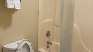 A bathroom with a toilet, a bathtub, and a shower. There are towels on a rack above the toilet.