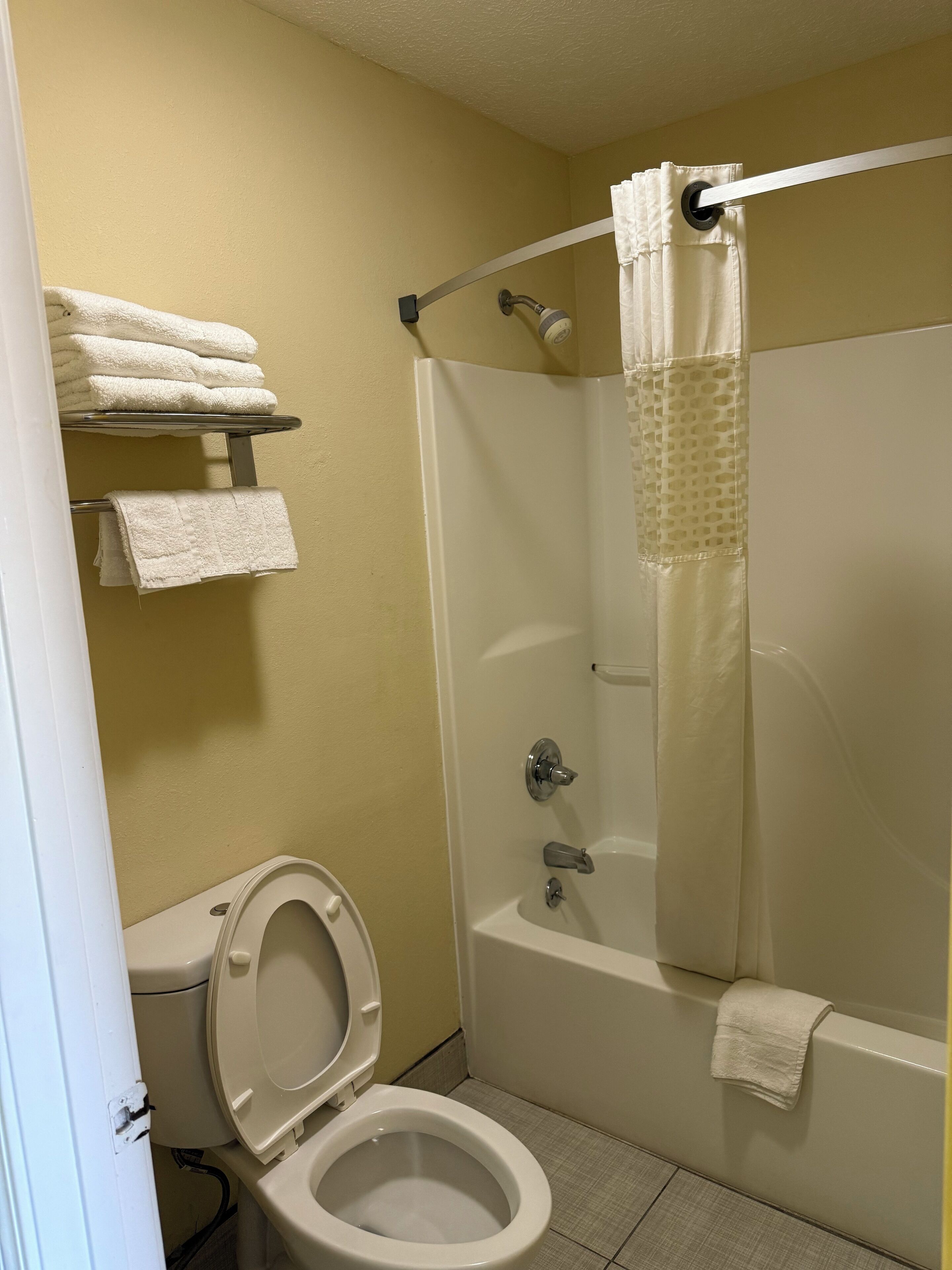 A bathroom with a toilet, a shower with a glass door, and a towel rack with folded towels.