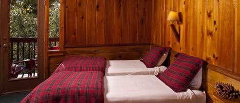 Habitación tipo cabaña con dos camas, una pared de madera, una ventana y una mesita de noche con lámpara.