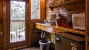 A wooden cabin kitchen with a stone tile floor, a refrigerator, a microwave, a coffee maker, and a window with a plaid curtain. - Idyllwild Bunkhouse (Idyllwild)