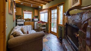 A cozy living room with a fireplace, wooden ceiling, and a stone fireplace surround. - Idyllwild Bunkhouse (Idyllwild)