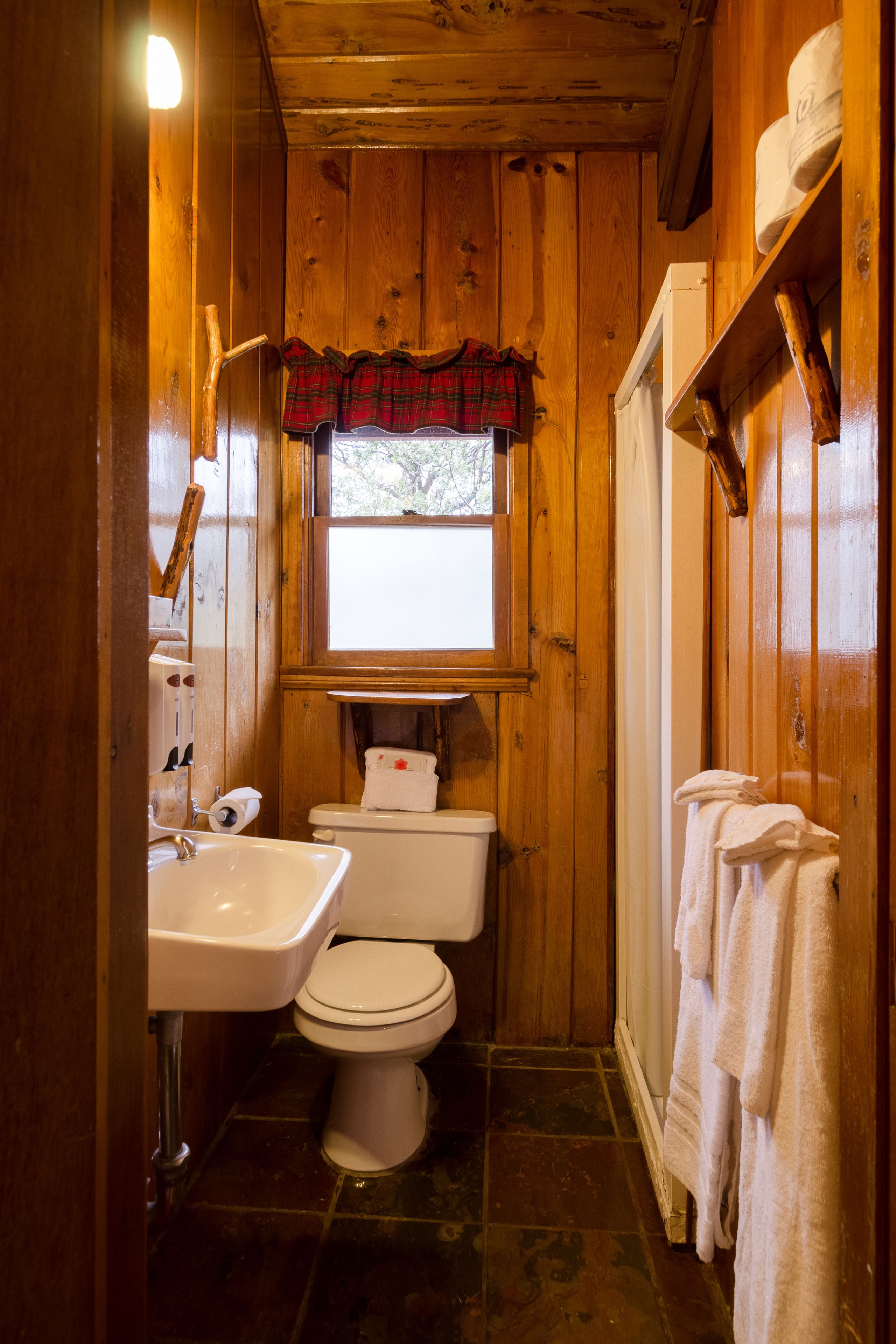 Baño de una cabaña de madera con lavamanos, inodoro y ventana.