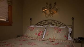 Una cama con ropa de cama floral, un aplique de pared y una ventana con persianas.