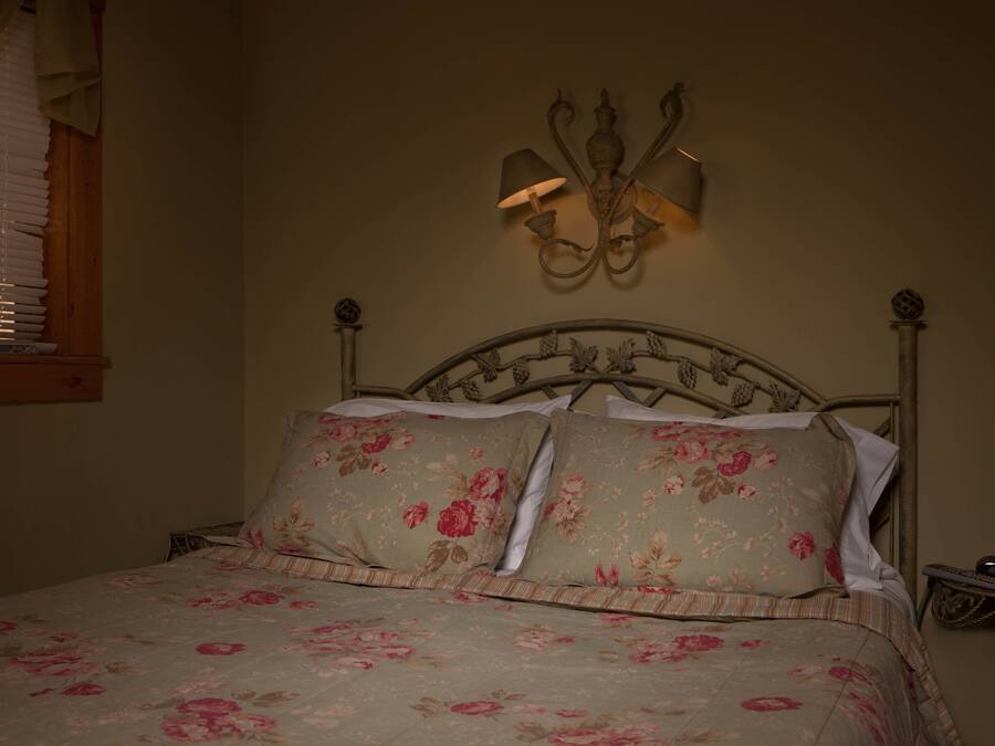 A bed with floral bedding, a wall-mounted light fixture, and a window with blinds.