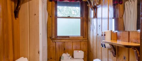 Baño de cabaña de madera con inodoro, lavamanos y ventana con cortina escocesa.