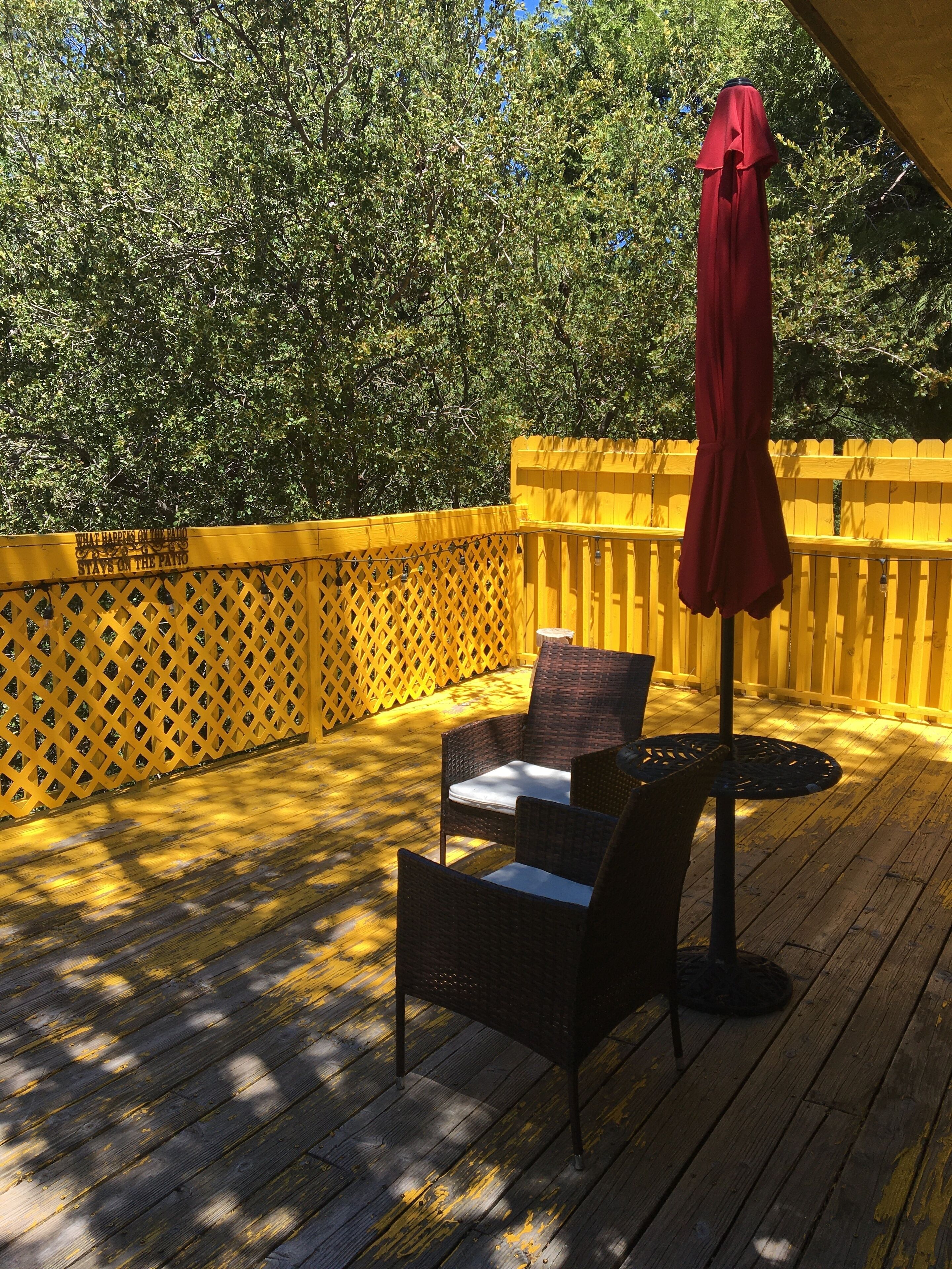 Una terraza de madera con muebles de mimbre y un paraguas rojo.