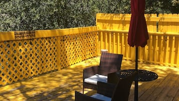 Une terrasse en bois avec des meubles en osier et un parasol rouge.