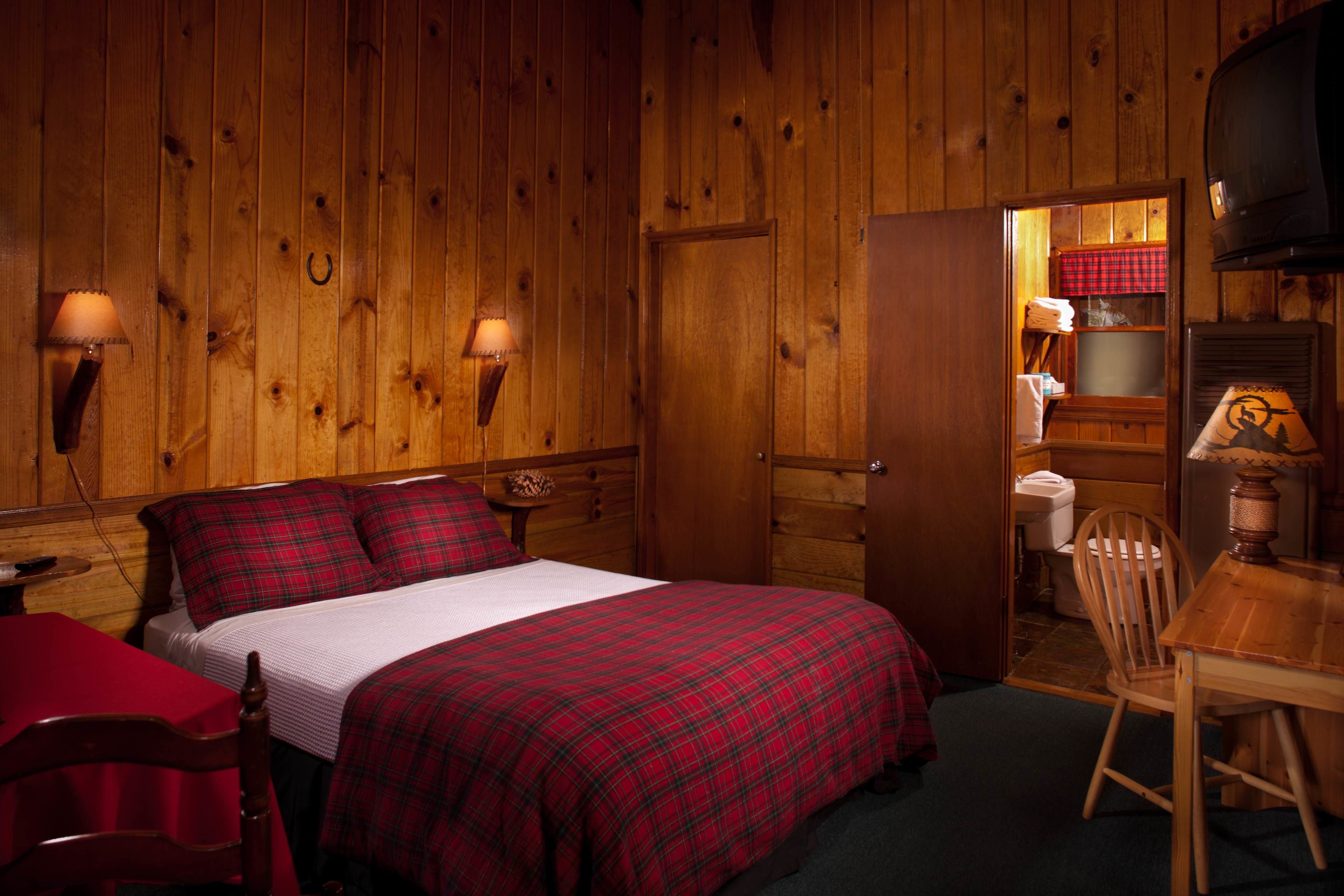 A wooden cabin room with a bed, a table, a chair, and a fireplace.