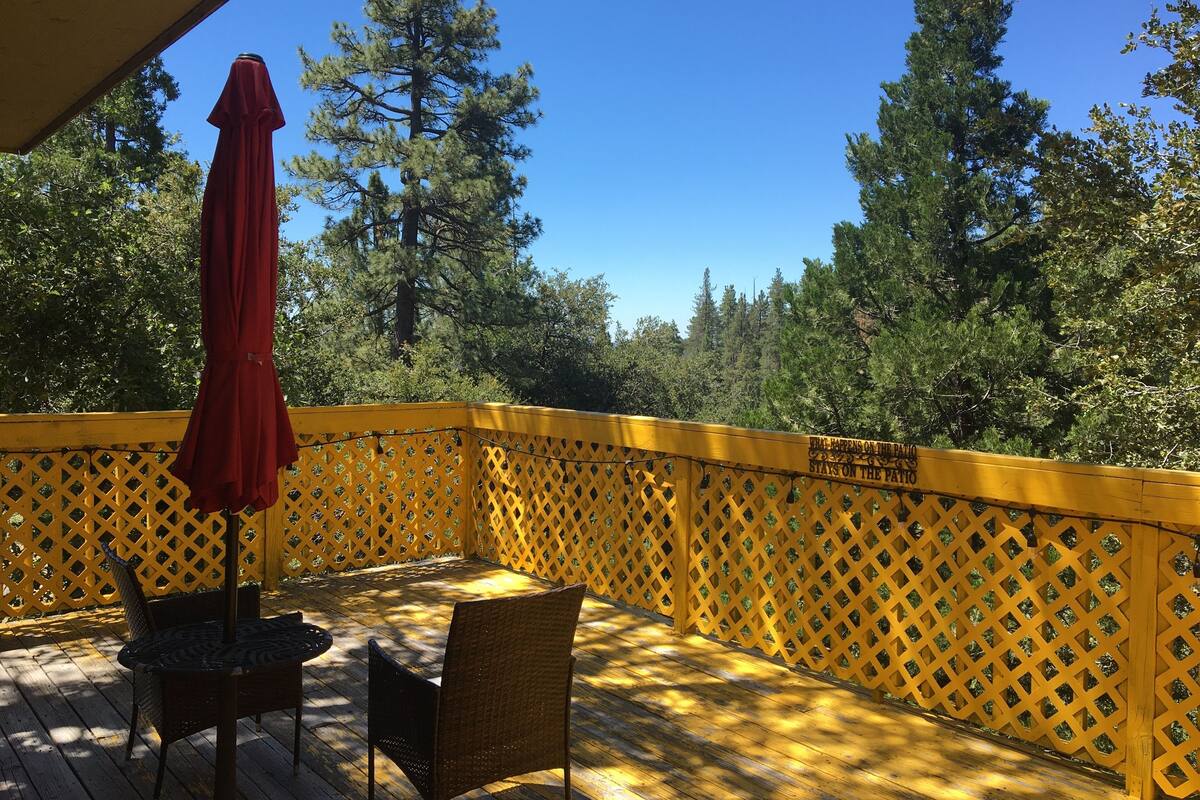 A wooden deck with a yellow lattice railing, a red umbrella, and a wicker chair.