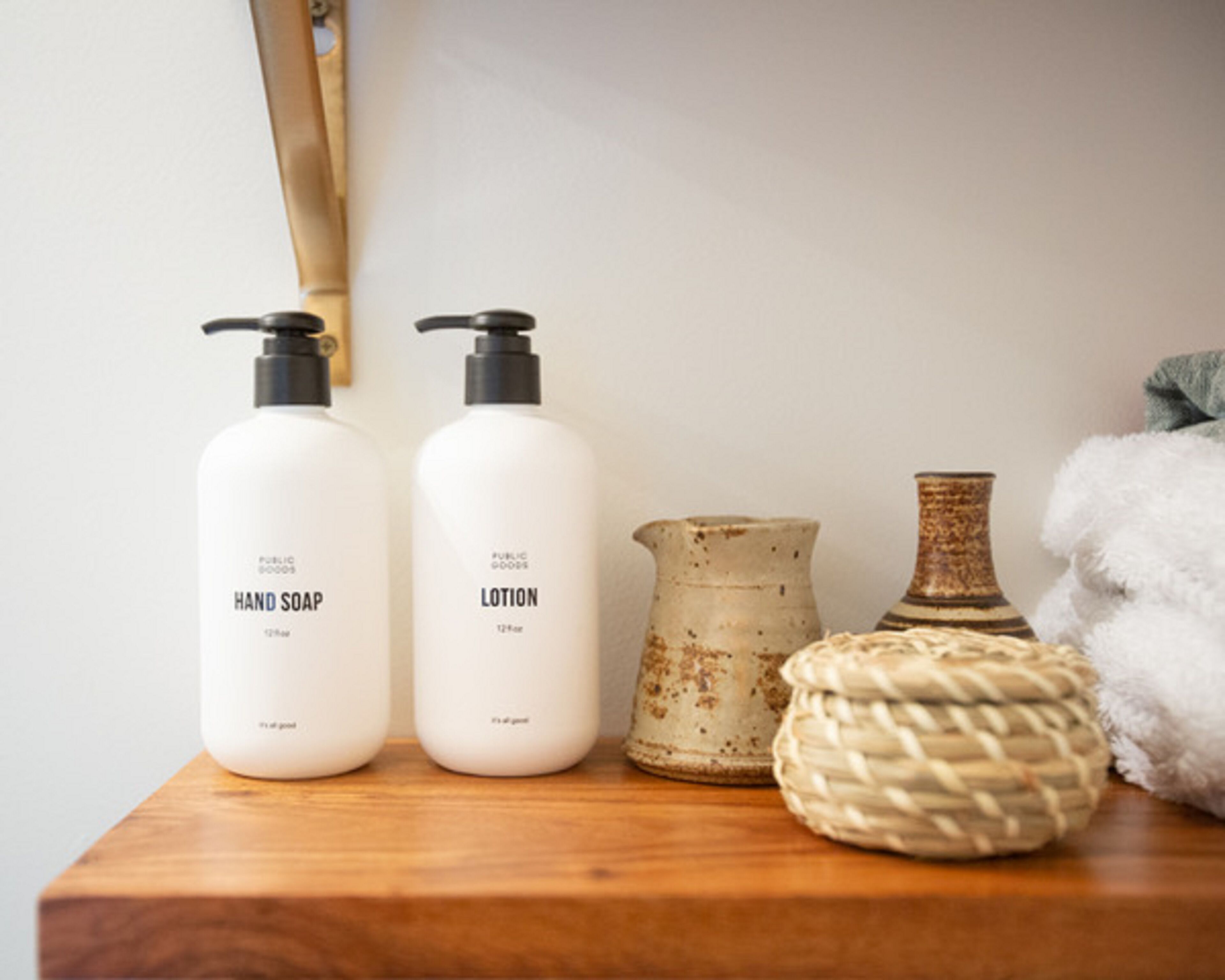 Two bottles of hand soap and lotion on a wooden surface, accompanied by a rustic vase and a woven basket.