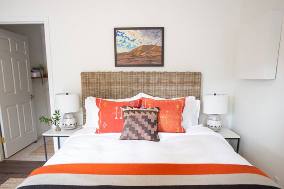 Habitación de hotel con una cama grande, dos lámparas de noche, un cabecero de mimbre y un cuadro en la pared.