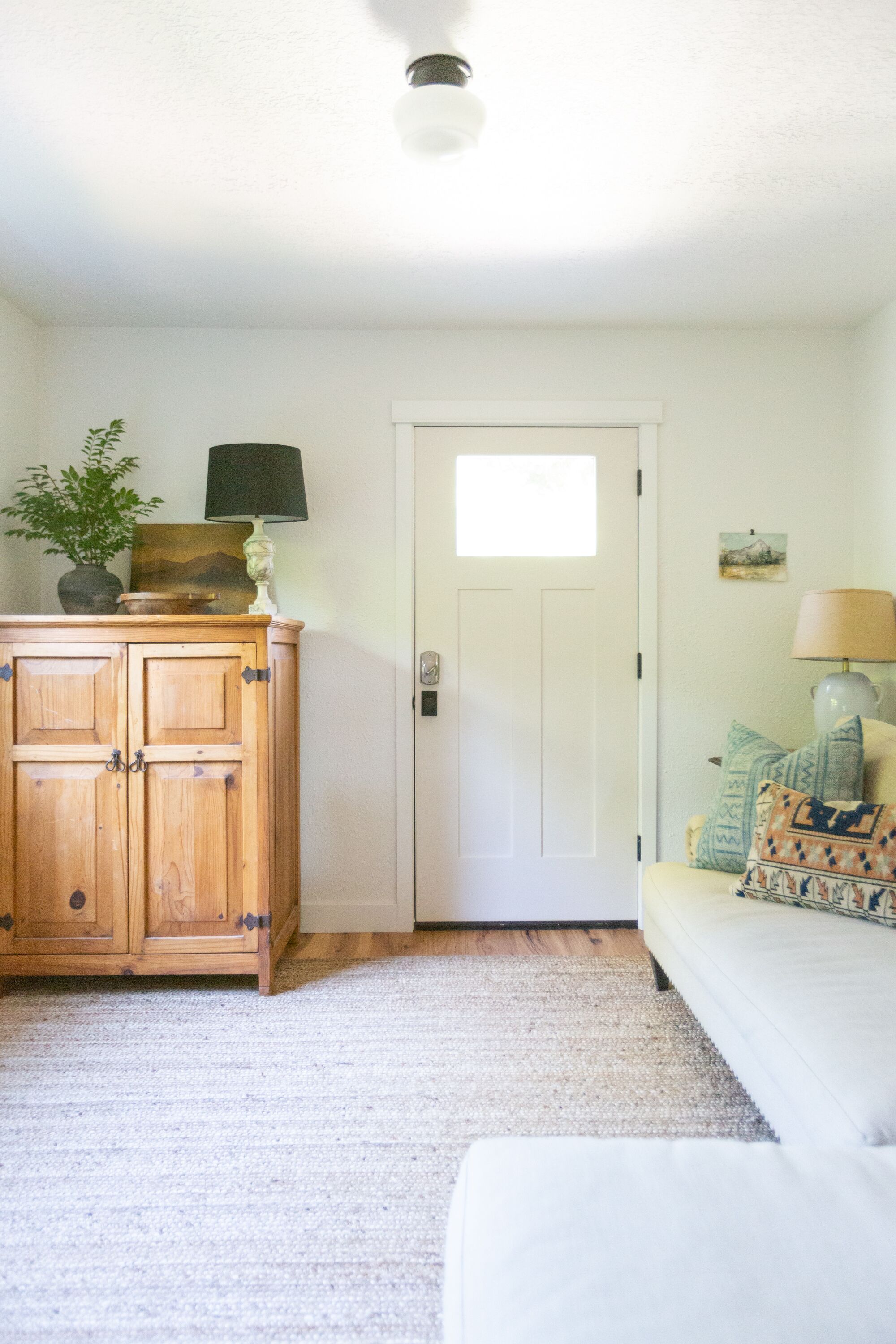 A room with a wooden cabinet, a white door, a beige sofa, and a small table with a lamp.