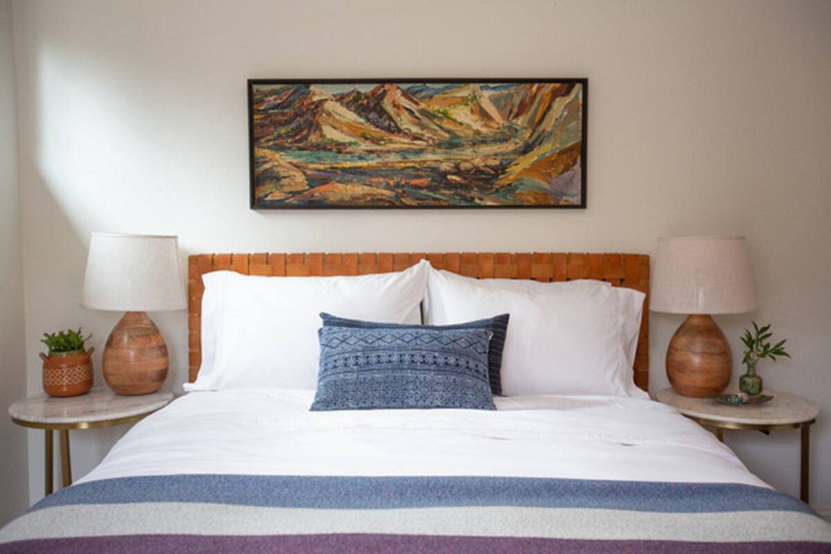 Una habitación de hotel con una cama grande, dos mesitas de noche, un cuadro en la pared y una ventana.